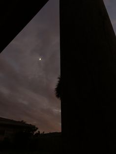 the moon is seen through some clouds in the night sky over a building and palm trees