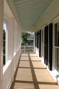 the sun shines through black shutters onto a porch with white walls and wood flooring