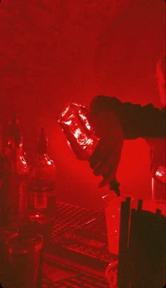 a person holding a glass in front of bottles on a bar with red light coming from behind it