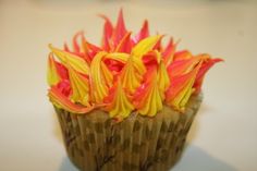 a cupcake with orange and yellow frosting on it's top sitting on a table