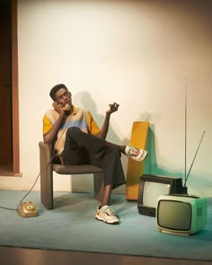 a man sitting in a chair next to an old fashioned tv and two small speakers