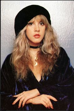 a woman with long hair wearing a black hat and dress is posing for a photo