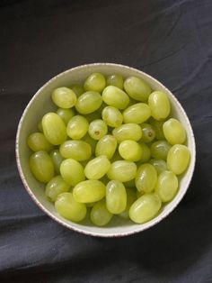 a white bowl filled with green grapes on top of a black table