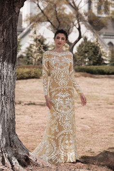 a woman standing in front of a tree wearing a dress with long sleeves and an open back