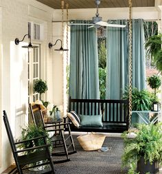 a porch with rocking chairs and potted plants on the front porch, along with blue curtains