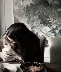 a woman sitting at a table with a bowl of food in front of her face