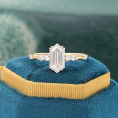 an emerald cut diamond engagement ring on top of a blue velvet cushion with yellow ribbon