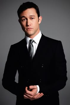 a man in a black suit and tie posing for a photo with his hands on his hips