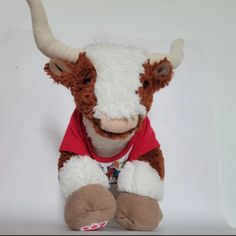 a brown and white stuffed cow wearing a red t - shirt sitting on a white surface