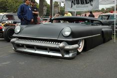 two men standing next to an old black car