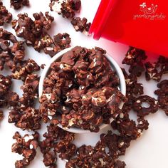 a white bowl filled with chocolate and nuts next to a red container full of peanuts