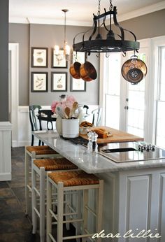 a kitchen island with stools and pots hanging from it's hooks, in front of a dining room table