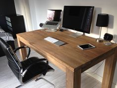 a wooden desk topped with two computer monitors and a laptop next to a black chair