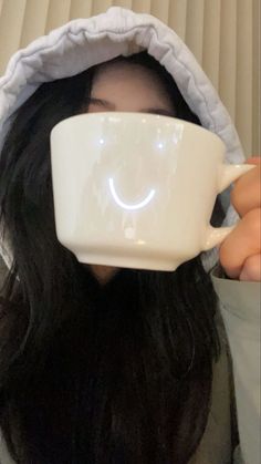 a woman with long black hair is holding a coffee cup in front of her face