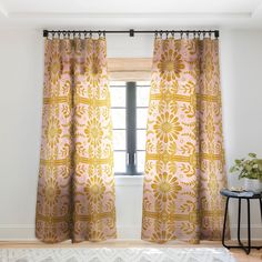 the curtains are hanging in front of a window with an ornate pattern on it, along with a rug and side table