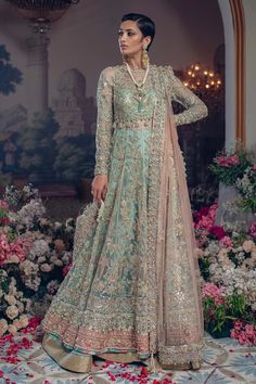 a woman standing in front of flowers wearing a green and gold lehenga suit