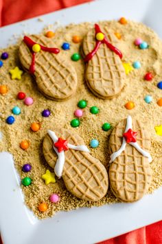 cookies decorated with candy and bows on a white platter covered in sand, sprinkles and colored candies