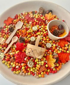 a white bowl filled with candy corn and wooden spoons next to an orange maple leaf