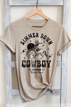 SIMMER DOWN COWBOY GRAPHIC TEE     Our Shirts are Authentically Designed and Hand Screen Printed for Best Quality    *Process where the ink is dyed into the shirt and graphic will not peel away     -Proudly Hand Pressed in Los Angeles, CA.     -30 Singles. 100% Washed Cotton     -Comfortable and Very Soft    -Style by Rolling up the Sleeves, Tie a Side Knot, Front Tuck...       SIZE AND FIT      *Please refer to the last photo option for measurements    WASHING AND CARE    -Machine Wash with Lik Southern Tshirt Ideas, Country Shirts For Women, Western Tshirt Designs, Western Shopping, Western Tee Shirts, Western T Shirts, Western Tees, Country Graphic Tees, Cowboy Graphic