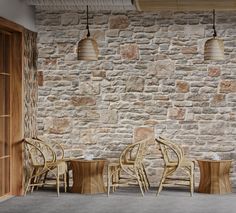 an empty room with chairs and tables in front of a stone wall that has hanging lamps above it