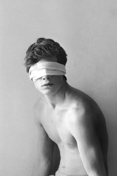 a shirtless man with a blindfold on his face is leaning against a wall