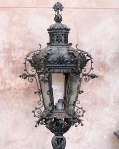 an old fashioned street light with ornate iron work on the top and bottom, standing against a stucco wall