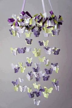 purple and green butterflies are hanging from a string on a gray background with white ribbons