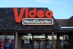 the front of a video headquarter store with its neon sign on it's roof