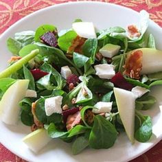 a white bowl filled with salad on top of a red table cloth next to a fork and knife