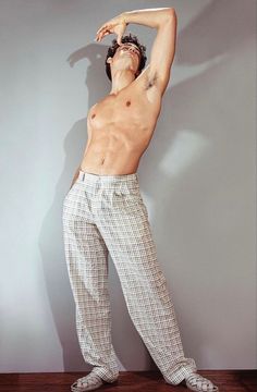 a man with no shirt on standing in front of a wall and stretching his arms