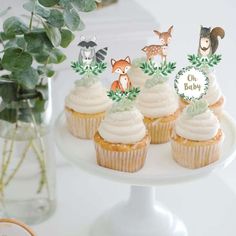 cupcakes with frosting and woodland animals are on a white cake platter