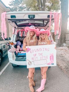 two women standing in the back of a truck holding a sign that says rounding up the best little princess