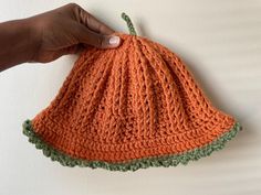 a hand is holding an orange crocheted dishcloth on a white surface with green trim