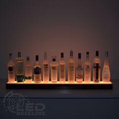 a row of liquor bottles sitting on top of a wooden shelf next to a wall