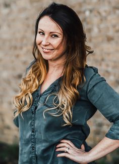 a woman standing in front of a brick wall with her hands on her hips and smiling