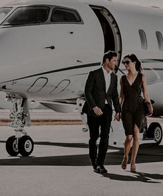 a man and woman walking towards an airplane on the tarmac with their hand in each other's pockets