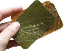 a hand holding a green leaf shaped business card with the words studio massage on it