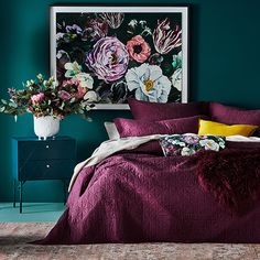 a bed in a room with green walls and purple bedspread, flowers on the headboard