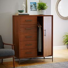 an armoire with clothes hanging on it next to a chair and potted plant