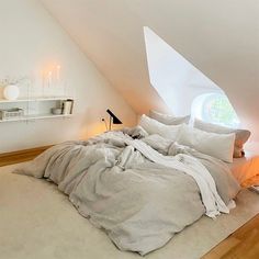 an unmade bed with white sheets and pillows in a loft space under a slanted ceiling