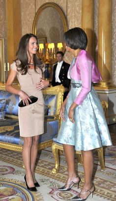 two women standing next to each other in front of a blue couch and gold chairs