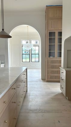 an arched doorway leads to a large kitchen with marble counter tops and white cabinets, along with a chandelier hanging from the ceiling