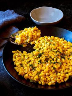 a black plate topped with corn on top of a table next to a white bowl