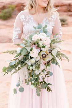 a woman in a pink dress holding a bouquet with greenery and flowers on it