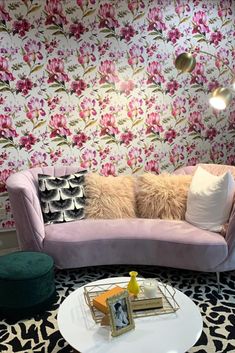 a living room with floral wallpaper and pink couches, coffee table and ottoman