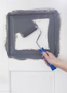 a person using a paint roller to paint a square frame on a wall with gray paint