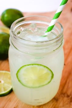 a mason jar filled with lemonade and limes on top of a wooden cutting board