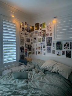 an unmade bed in a bedroom with many pictures on the wall and lights above it