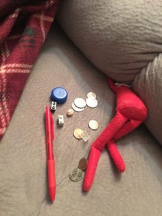 a red stuffed animal sitting on top of a couch next to coins and a pen