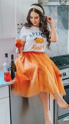 a woman in an orange tulle skirt and t - shirt sitting on top of a refrigerator